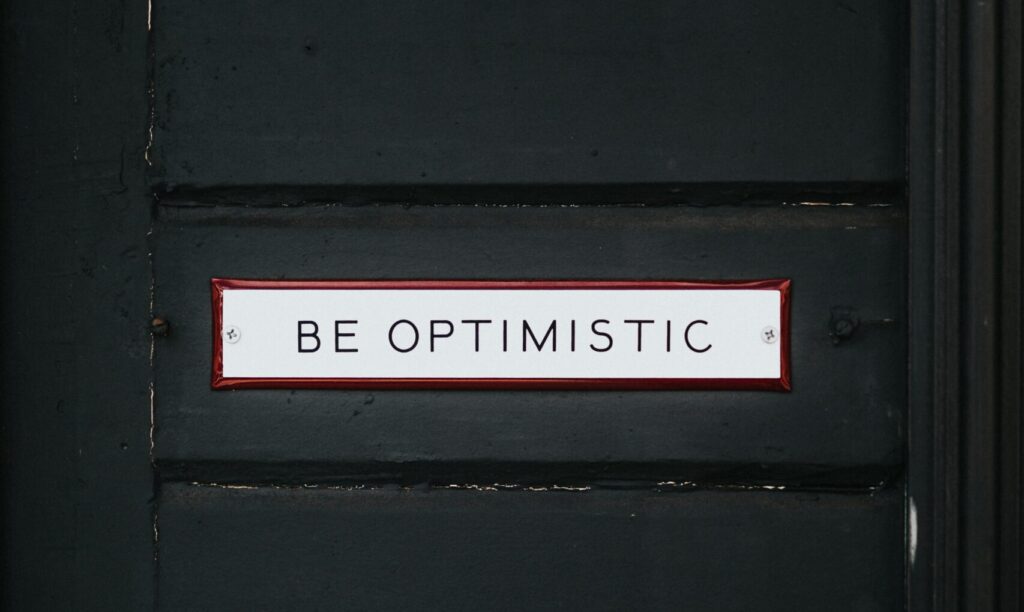 black wooden door with be optimistic text overlay