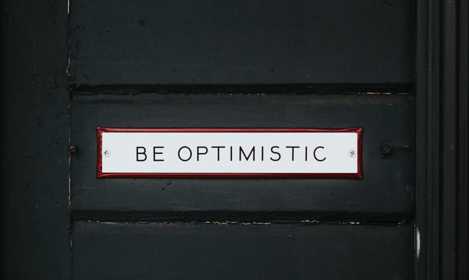 black wooden door with be optimistic text overlay